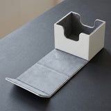 A white deck box sits open on a dark gray tabletop, revealing gray lining and an extended front flap.