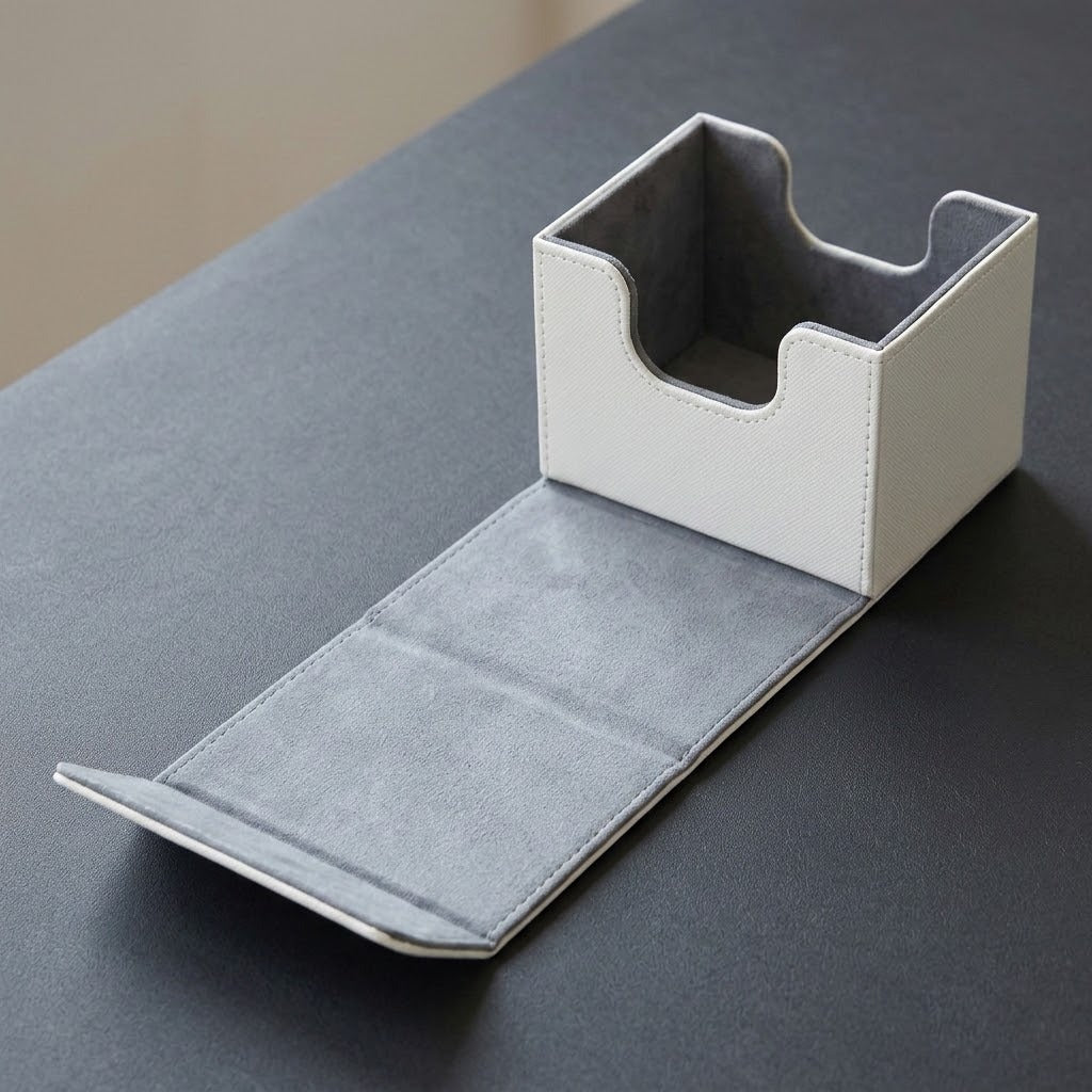 A white deck box sits open on a dark gray tabletop, revealing gray lining and an extended front flap.