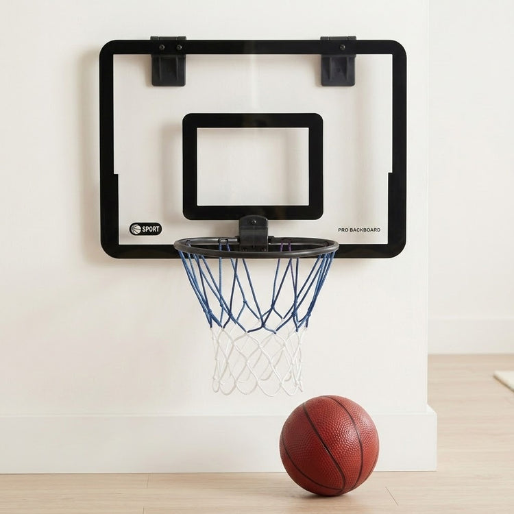 A wall-mounted basketball hoop with a clear backboard, black rim and frame, blue net, and a basketball on a light wood floor against a white wall.