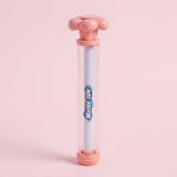 A pink and clear water gun with a white inner tube and flower-shaped handle stands upright against a pale pink background.