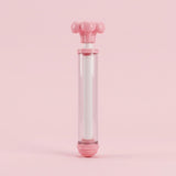 A pink and clear water gun with its flower-shaped handle slightly extended stands upright against a solid pink background.