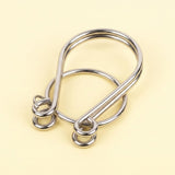 Silver metal loop puzzle from the brain teaser set, with interlocking curved wires and a ring on a pale yellow background.