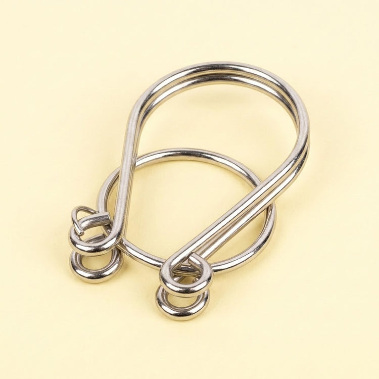 Silver metal loop puzzle from the brain teaser set, with interlocking curved wires and a ring on a pale yellow background.