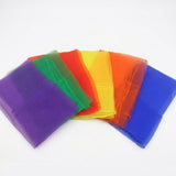 Six folded chiffon juggling scarves in purple, green, red, yellow, orange and blue overlap in a fan on white.
