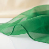 A close-up of a sheer green fabric scarf or sash draped elegantly, showing its lightweight texture and fine weave against a soft, light beige and white background.