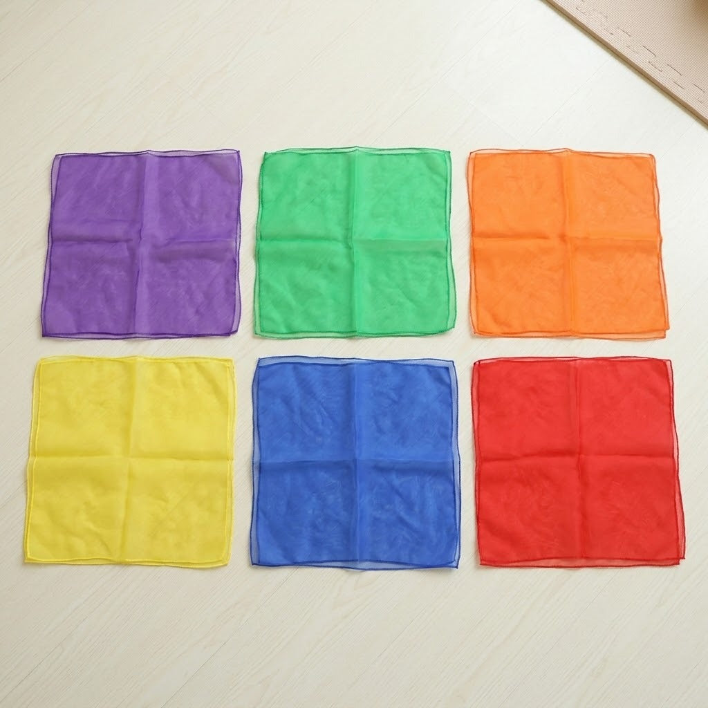 Six square chiffon juggling scarves in purple, green, orange, yellow, blue and red lie in two rows on a light surface.