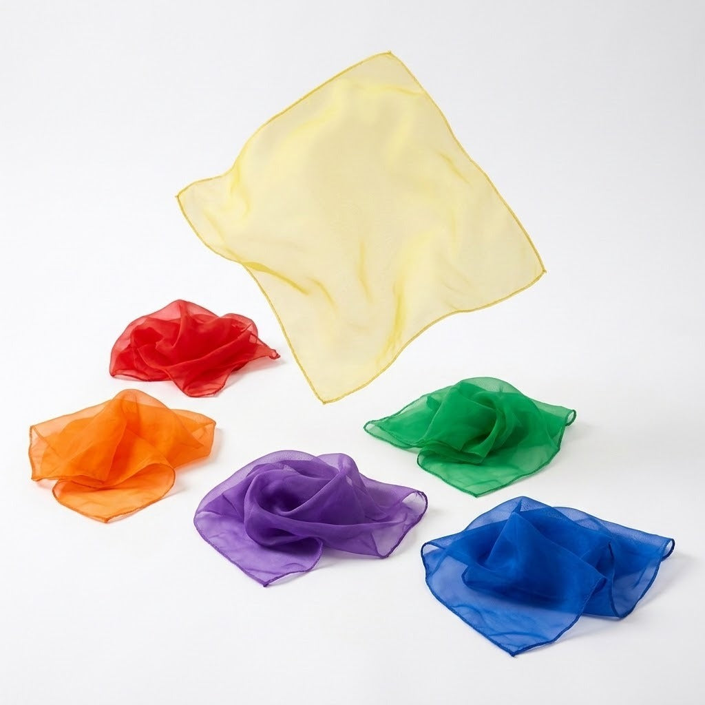 Six chiffon juggling scarves rest on a white background, with yellow spread above loosely gathered red, orange, green, purple, and blue scarves.