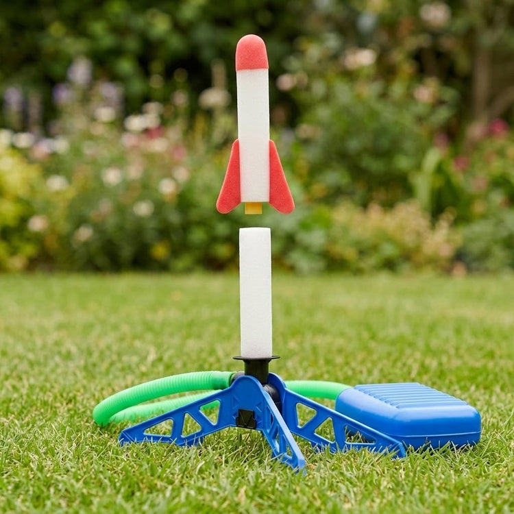 A plastic toy rocket launcher on grass, featuring a blue base with a green hose, a blue charging box, and a white rocket with red fins and a red nose cone.
