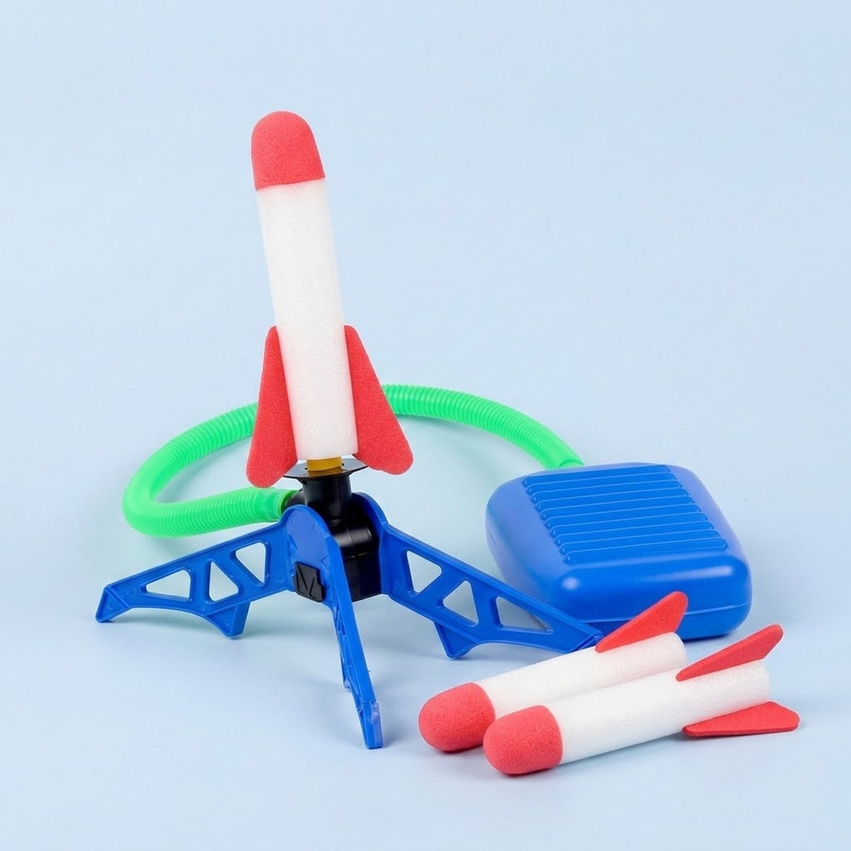 Rocket launcher toy with blue stand and foot pump, green hose, and three white rockets with red fins against a light blue background.