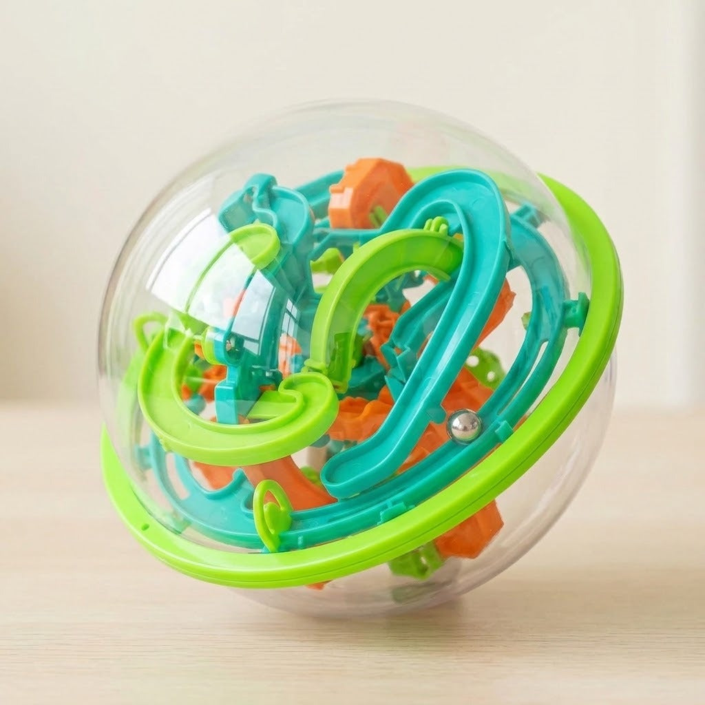 A maze puzzle on a light wooden surface shows curved teal and lime-green tracks and a steel ball inside its clear shell.
