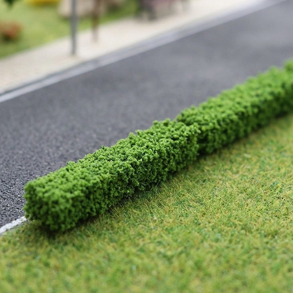 Green model hedges with dense textured foliage line a gray miniature road beside grassy terrain.