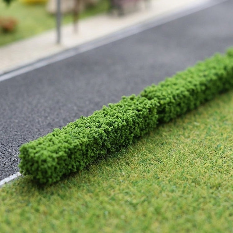 Green model hedges with dense textured foliage line a gray miniature road beside grassy terrain.
