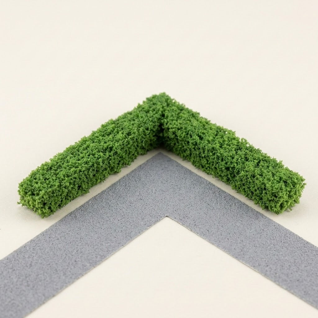 Two green miniature hedge strips form a right-angle corner beside a gray model path on a cream background.