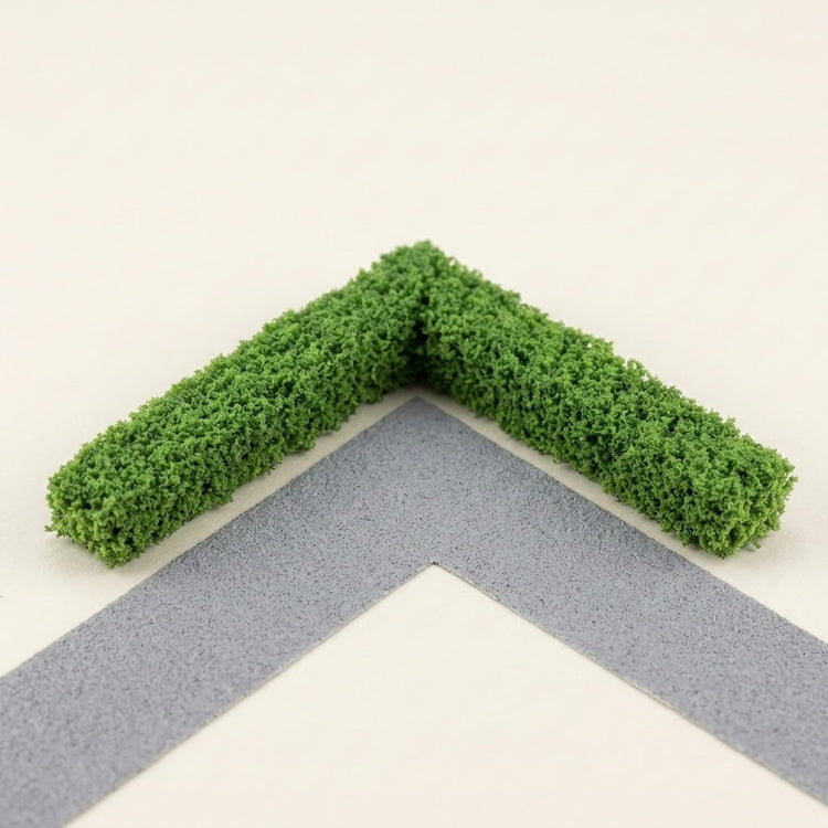 Two green miniature hedge strips form a right-angle corner beside a gray model path on a cream background.