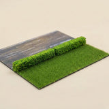Two green miniature hedge strips sit end to end between a model road and rectangular grass patch on a cream background.