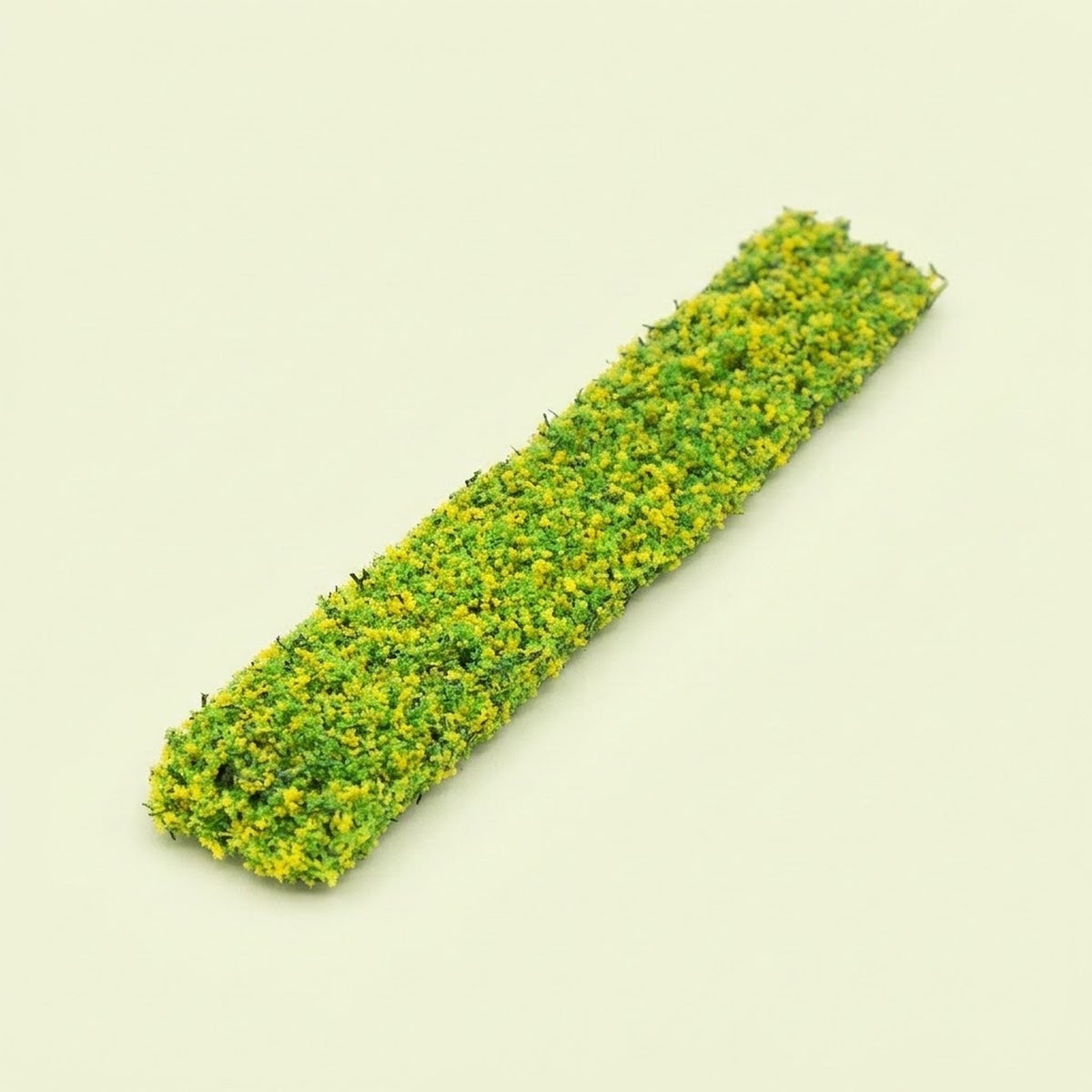 A miniature model hedge with yellow and green textured foliage lies diagonally on a pale yellow background.