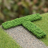 Green model hedges form a T-shaped arrangement beside a gravel path on miniature grassy terrain.