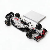 Assembled white and black car building set with red accents sits beside a closed gray booklet on a white background.