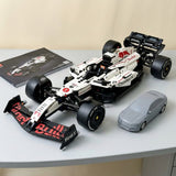 A white and black building-block toy Formula 1 race car with red Bull graphics, displayed on a light gray tabletop next to a gray toy car and a printed box insert.
