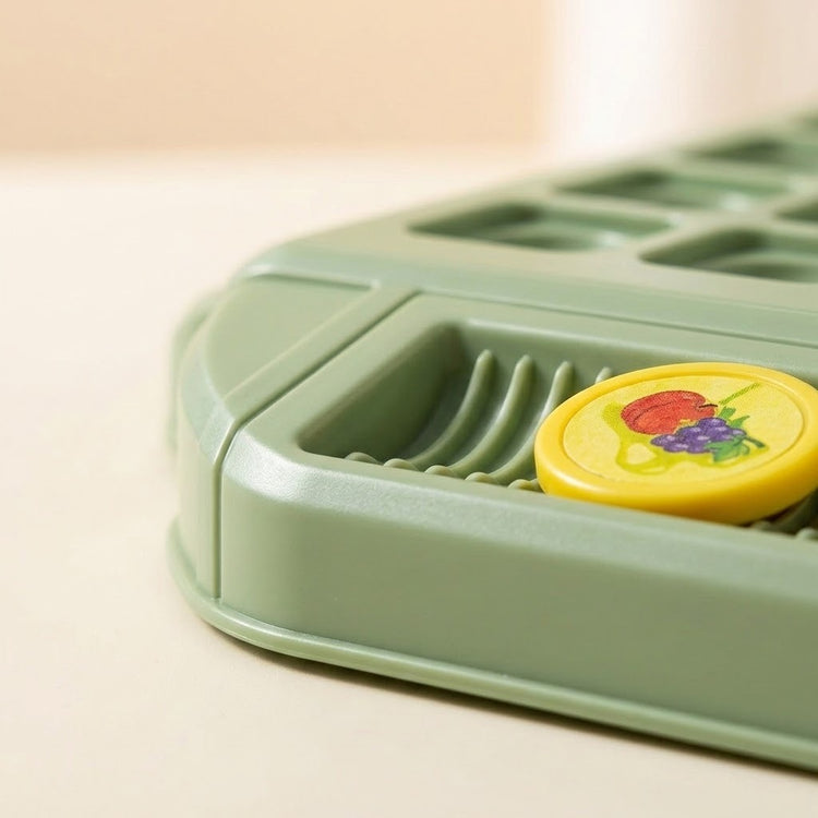 A close-up of the memory matching game shows a green plastic corner tray holding a yellow fruit piece against a beige background.