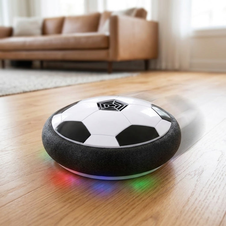 A black and white hover soccer ball with a textured foam bumper casts colored light onto a wooden living room floor.