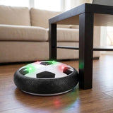 Black-and-white hover soccer ball with colorful LEDs and a foam bumper touching a dark table leg on a wooden floor.