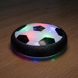 Black-and-white hover soccer ball with colorful LEDs glowing across its shell and reflecting on a wooden floor in dim lighting.