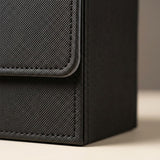 A close-up shows the black deck box's textured exterior, stitched flap, and lower corner on a beige surface.