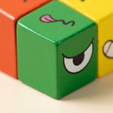 Close-up of a green expression matching game cube showing an eye and tongue detail beside red-orange and yellow cubes.