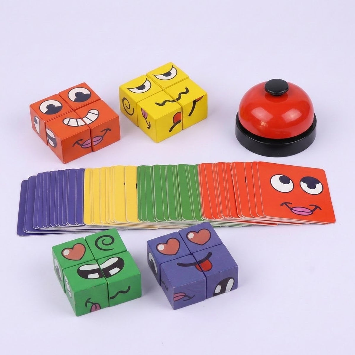 A colorful children's card and block game set on a light gray background, featuring four cube pieces with cartoon faces, a fan of matching cards, and a red bell.