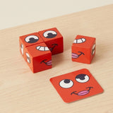 Face matching game with four red expression blocks and a red face card on a light wood tabletop.
