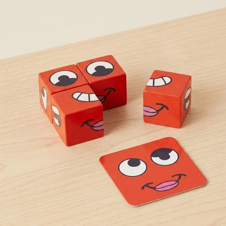Face matching game with four red expression blocks and a red face card on a light wood tabletop.