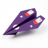Purple paper airplane folded from this origami kit, printed with white stars and red-and-white wing graphics, on a plain white background.