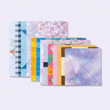 Overlapping origami kit paper sheets feature pastel floral, geometric, and cartoon patterns with printed folding lines on a pale lavender background.