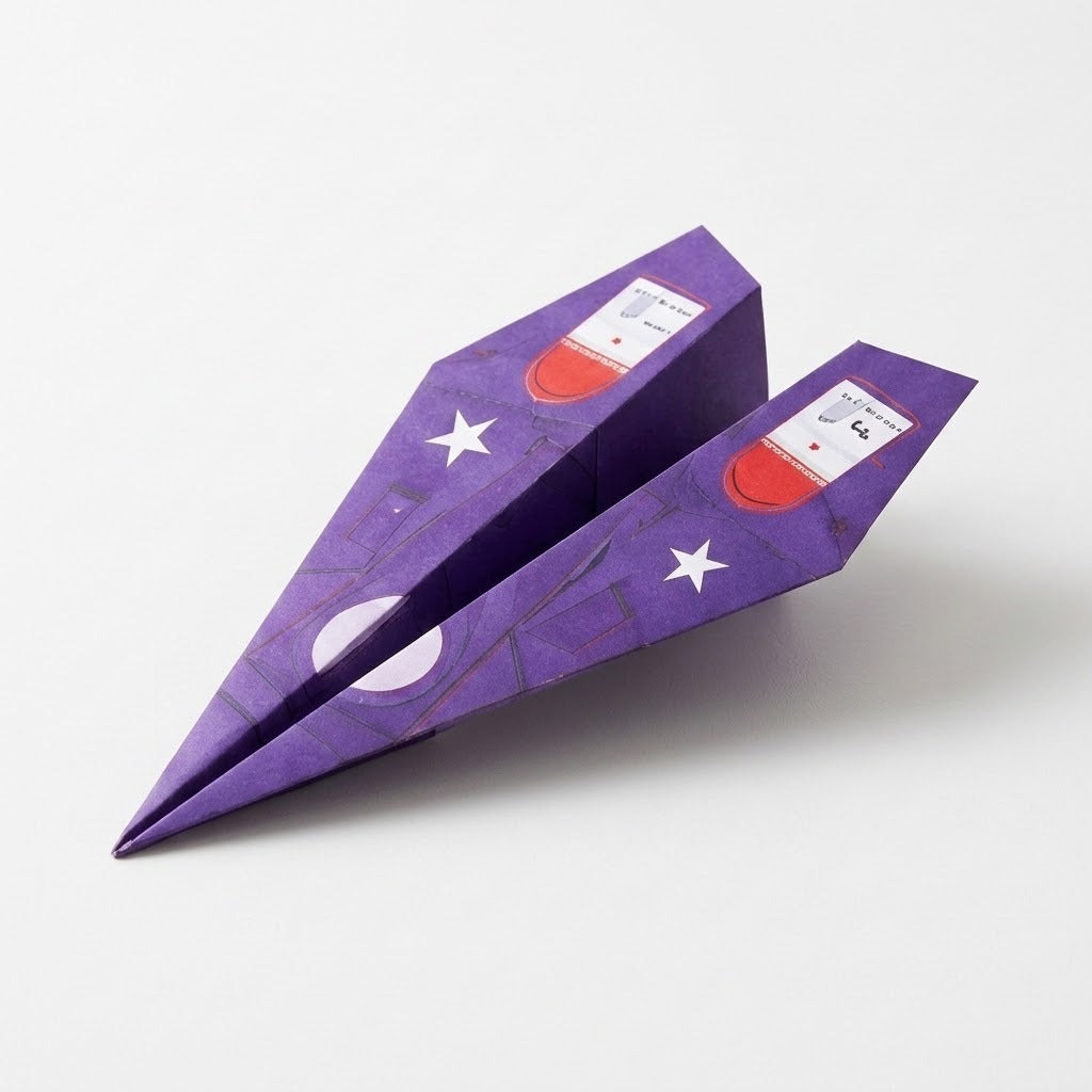 A purple paper airplane from the origami kit rests on white, decorated with white stars and red-and-white wing graphics.