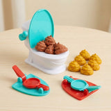 Tabletop game with a white toilet, turquoise lid, two colourful launchers, and brown and yellow toy poops on a light wood table.