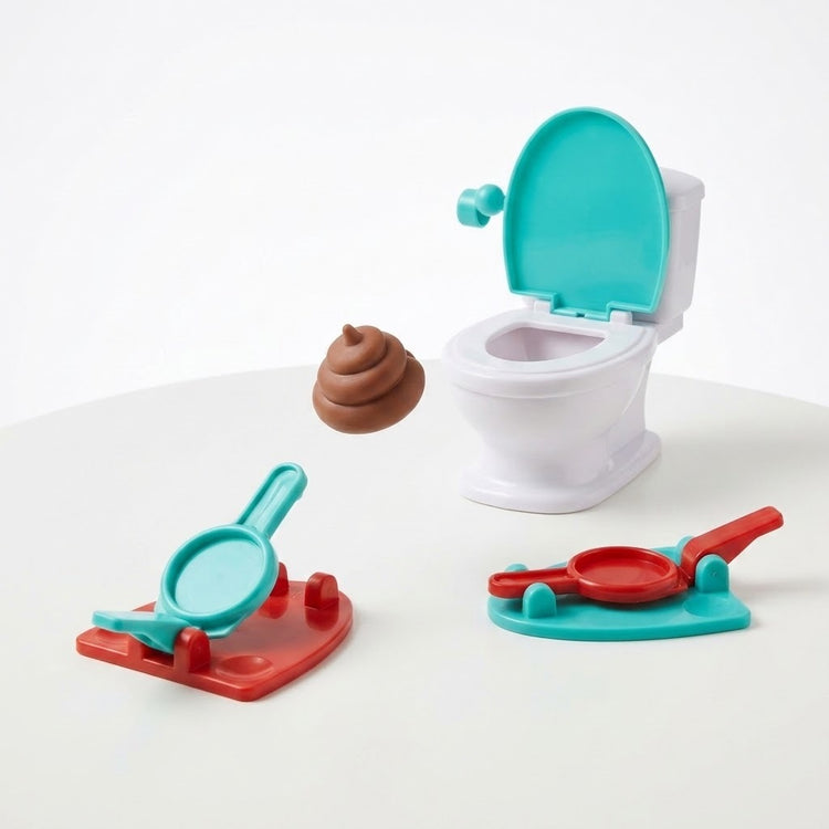 Tabletop game on a white background with a turquoise-lidded white toilet, two red and turquoise launchers, and a brown toy poop airborne.