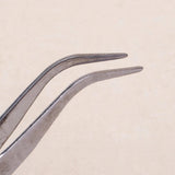 Silver metal tweezers with bent tips shown close up against a pale beige background.
