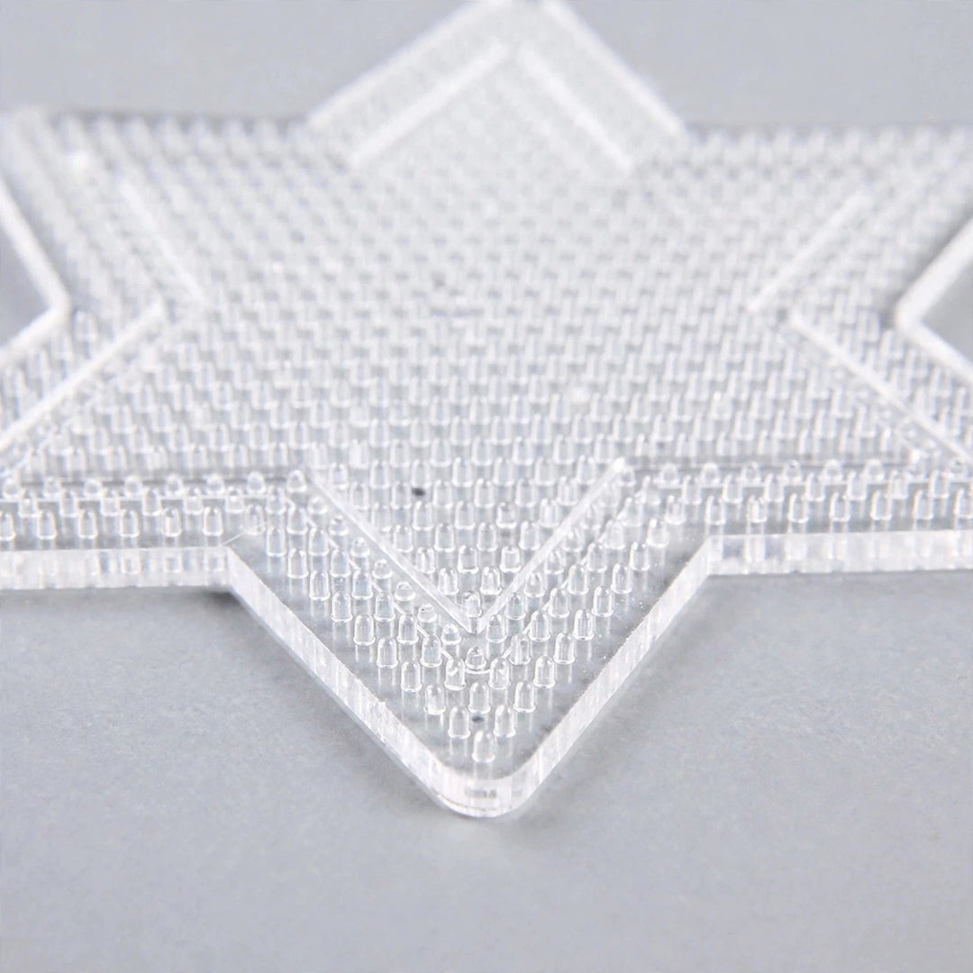 A clear star-shaped plastic bead pegboard with closely spaced pegs rests on a light grey surface.