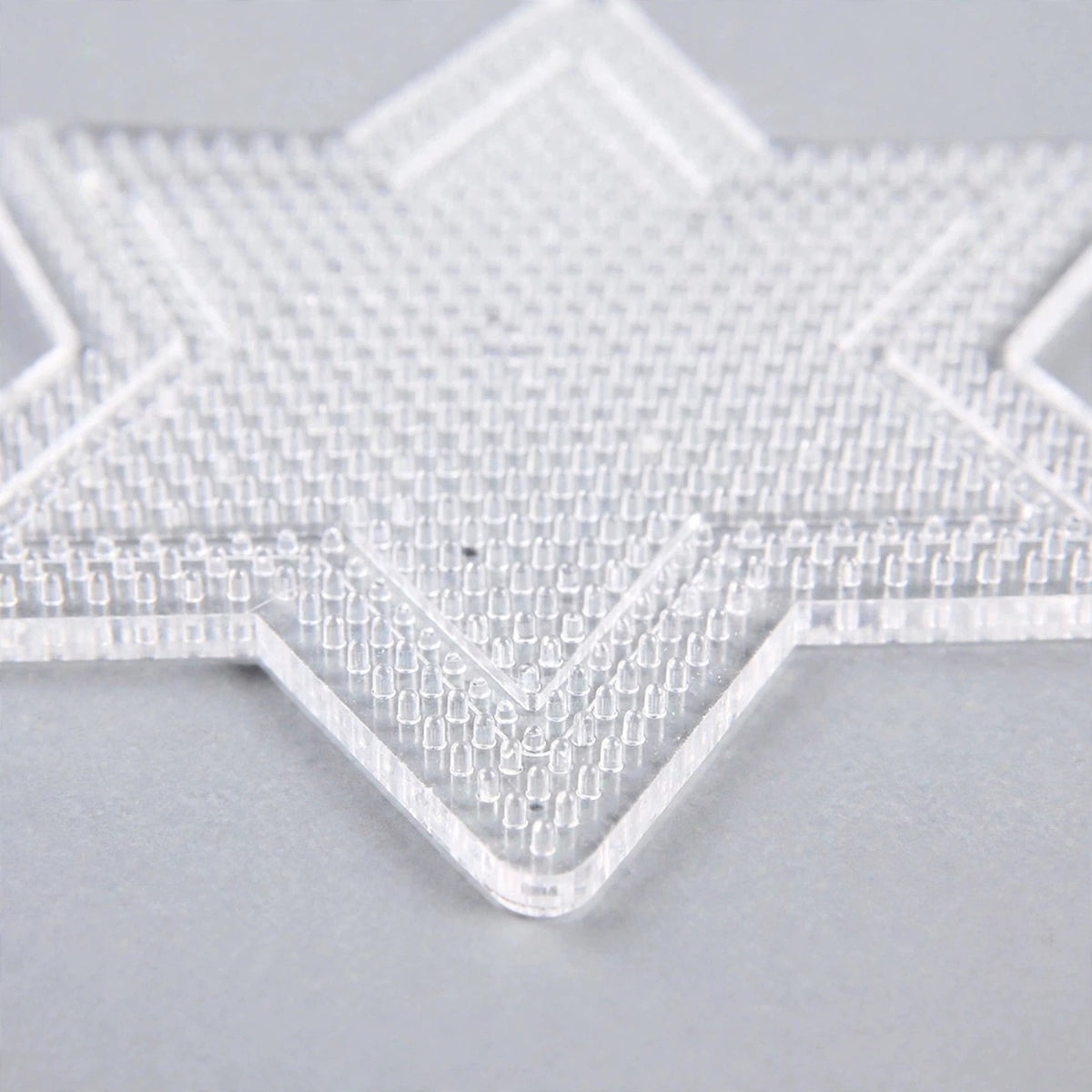 A clear star-shaped plastic bead pegboard with closely spaced pegs rests on a light grey surface.