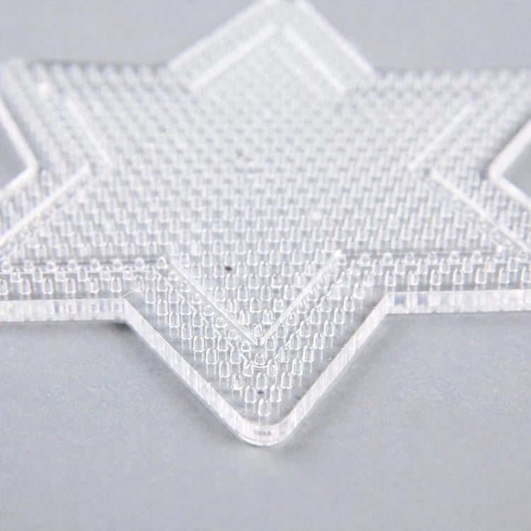 A clear star-shaped plastic bead pegboard with closely spaced pegs rests on a light grey surface.