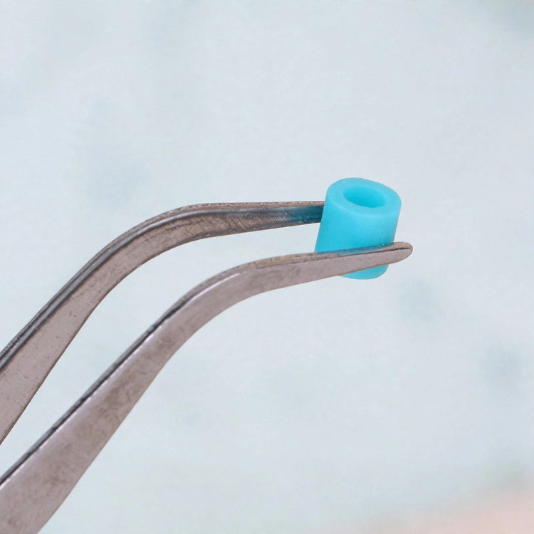 Bent silver metal tweezers hold a single turquoise cylindrical bead against a pale background.
