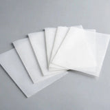Thin white square sheets overlap in a fan arrangement on a grey surface.