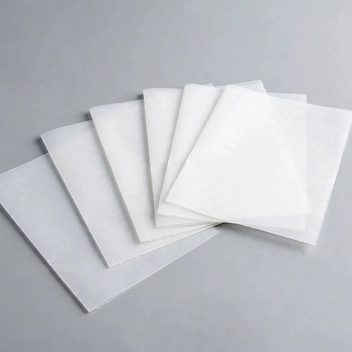 Thin white square sheets overlap in a fan arrangement on a grey surface.