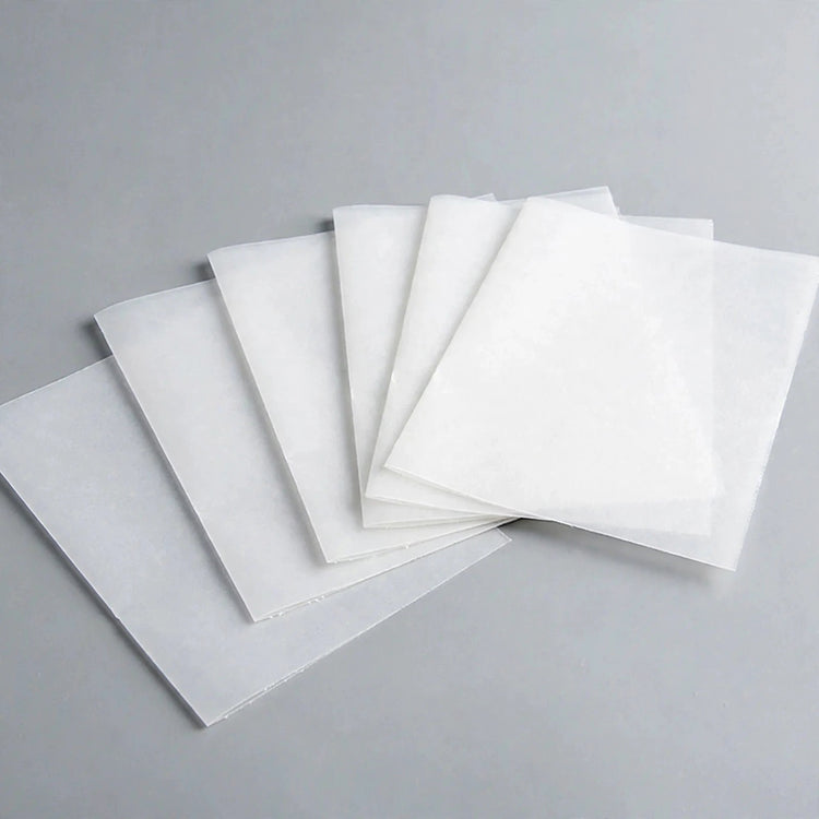 Thin white square sheets overlap in a fan arrangement on a grey surface.