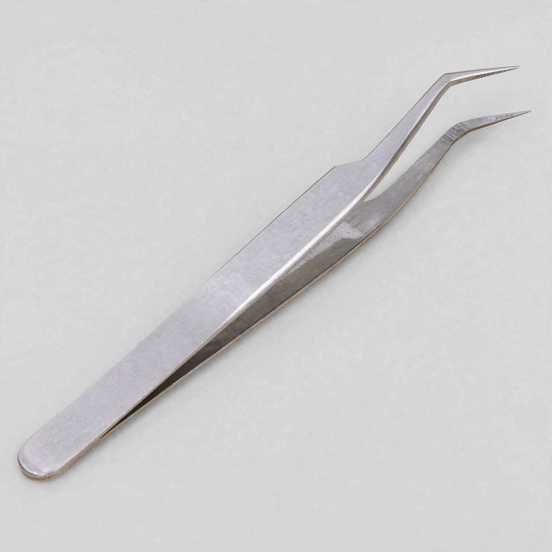 Silver metal tweezers with bent pointed tips lie diagonally on a light grey background.