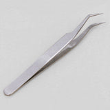 Silver metal tweezers with bent pointed tips lie diagonally on a light grey background.