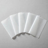 Five white rectangular ironing paper sheets overlap in a fan arrangement on a light grey surface.