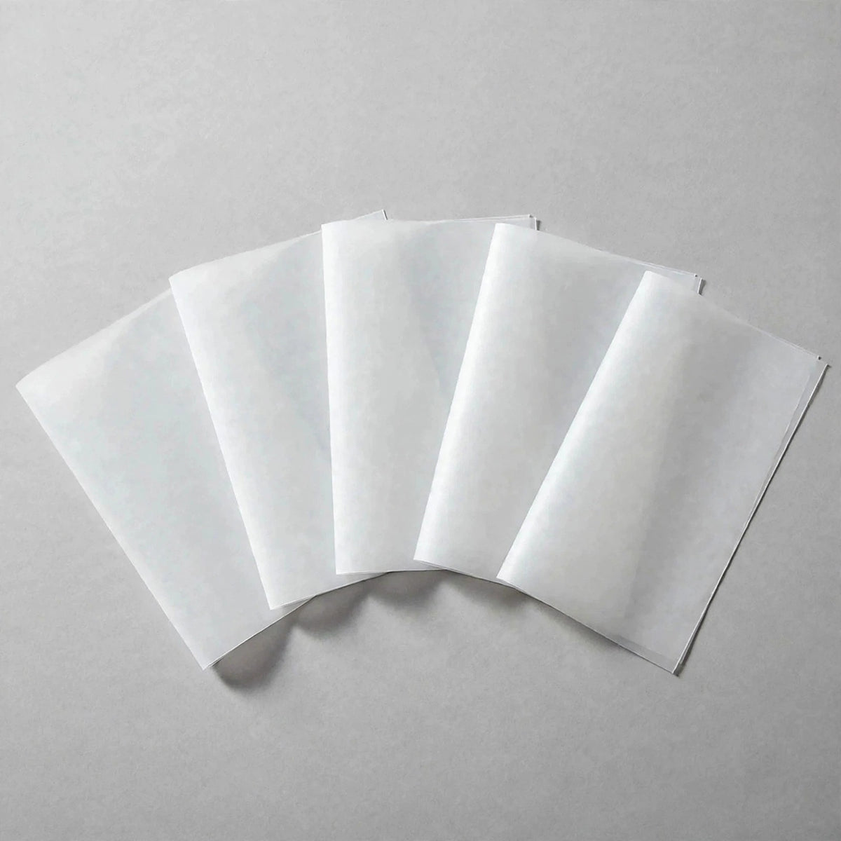 Five white rectangular ironing paper sheets overlap in a fan arrangement on a light grey surface.