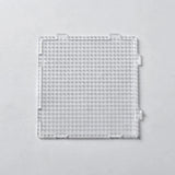 A clear square plastic bead pegboard with interlocking edge tabs is shown from above on a light grey background.